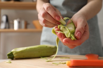 Photo of Woman with peels of fresh zucchini at table in kitchen, closeup. Space for text