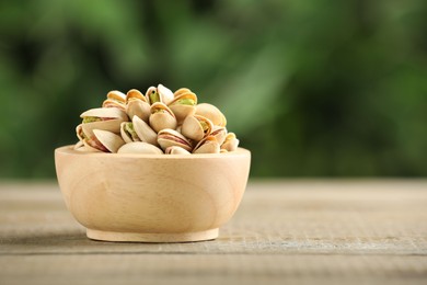 Photo of Tasty pistachios in bowl on wooden table against blurred background, closeup. Space for text