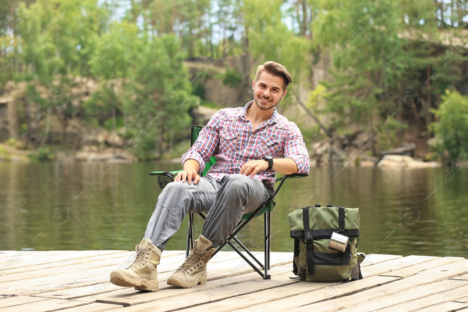 Photo of Young man resting on wooden pier near lake. Camping season