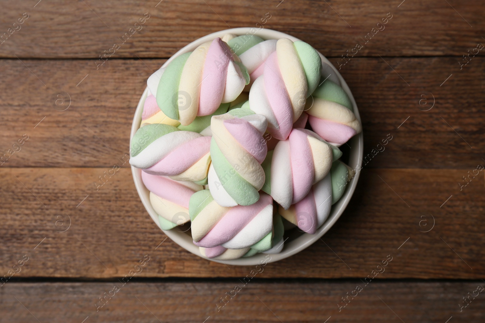 Photo of Bowl with colorful marshmallows on wooden table, top view