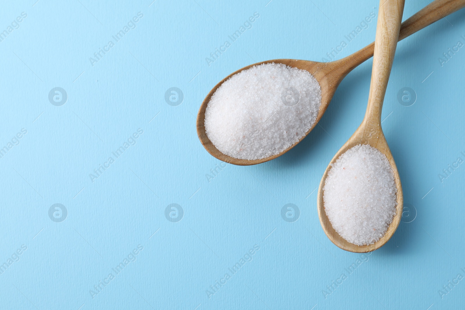 Photo of Organic white salt in spoons on light blue background, top view. Space for text