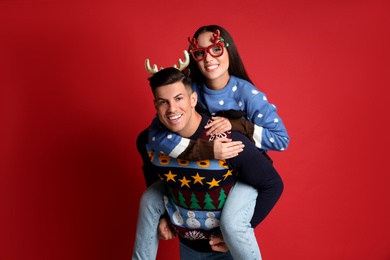 Photo of Couple in Christmas sweaters, deer headband and party glasses on red background