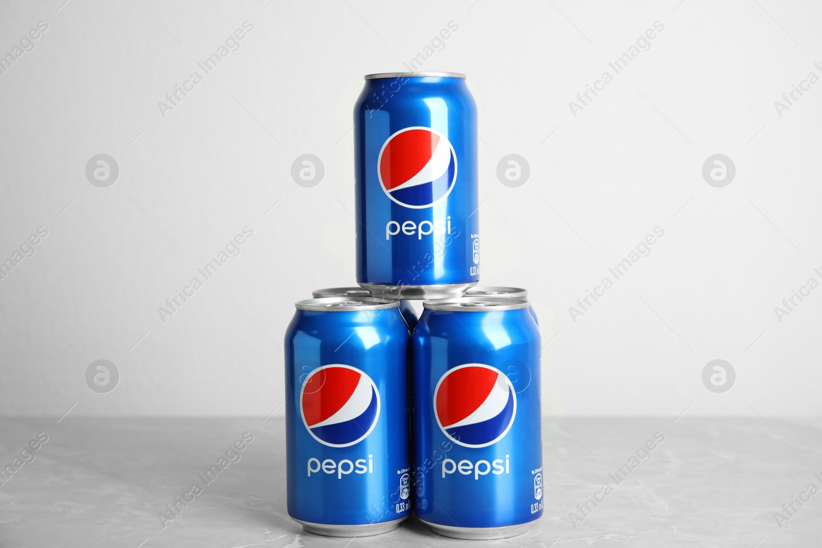 Photo of MYKOLAIV, UKRAINE - FEBRUARY 9, 2021: Cans of Pepsi on grey table against white background