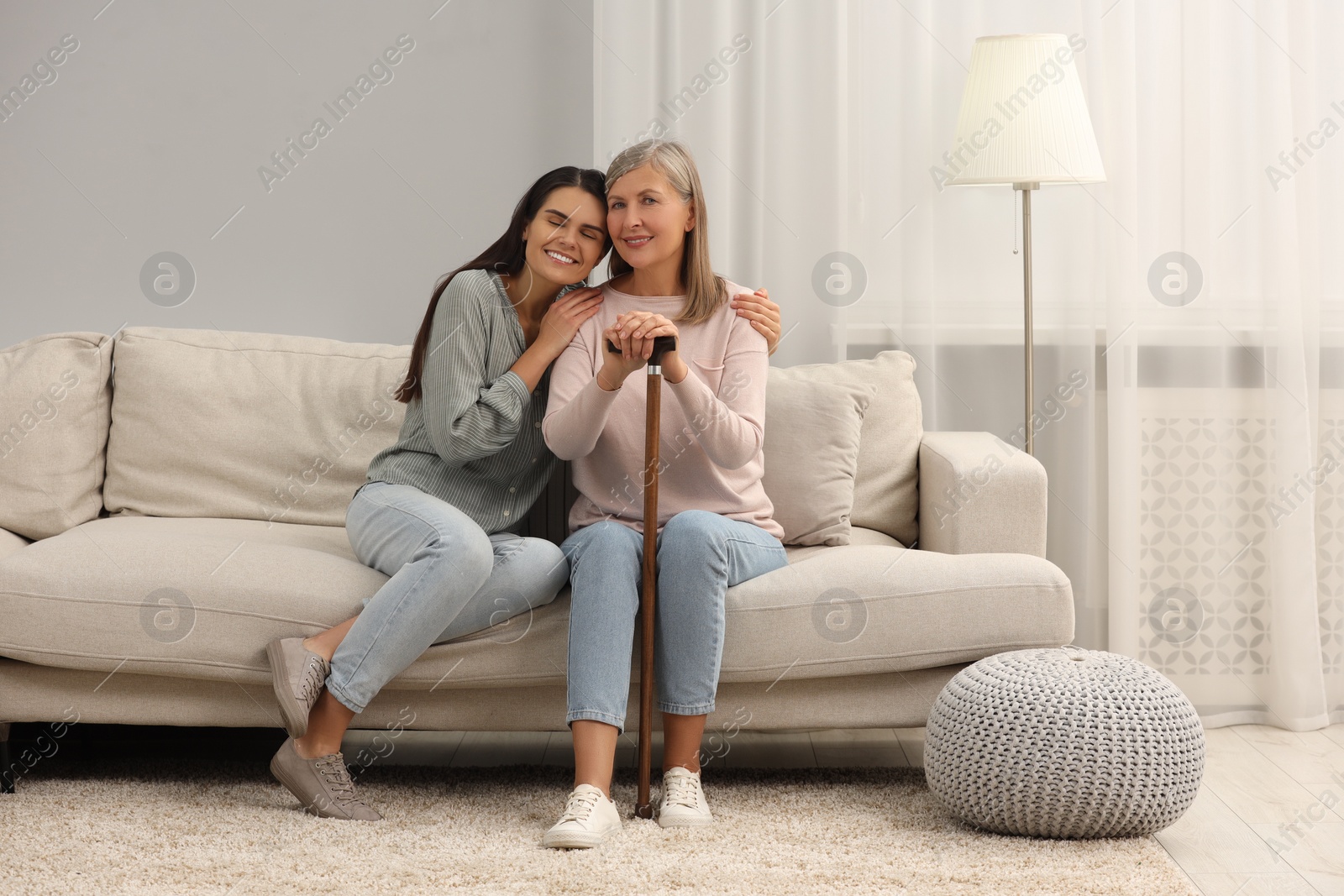 Photo of Mature lady with walking cane and young woman on sofa at home