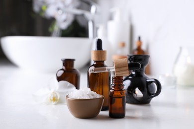 Photo of Essential oils and sea salt on white table in bathroom, closeup