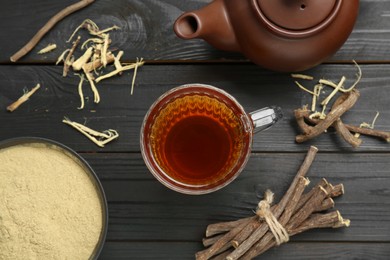 Aromatic licorice tea in cup, teapot, dried sticks of licorice root and powder on black wooden table, flat lay