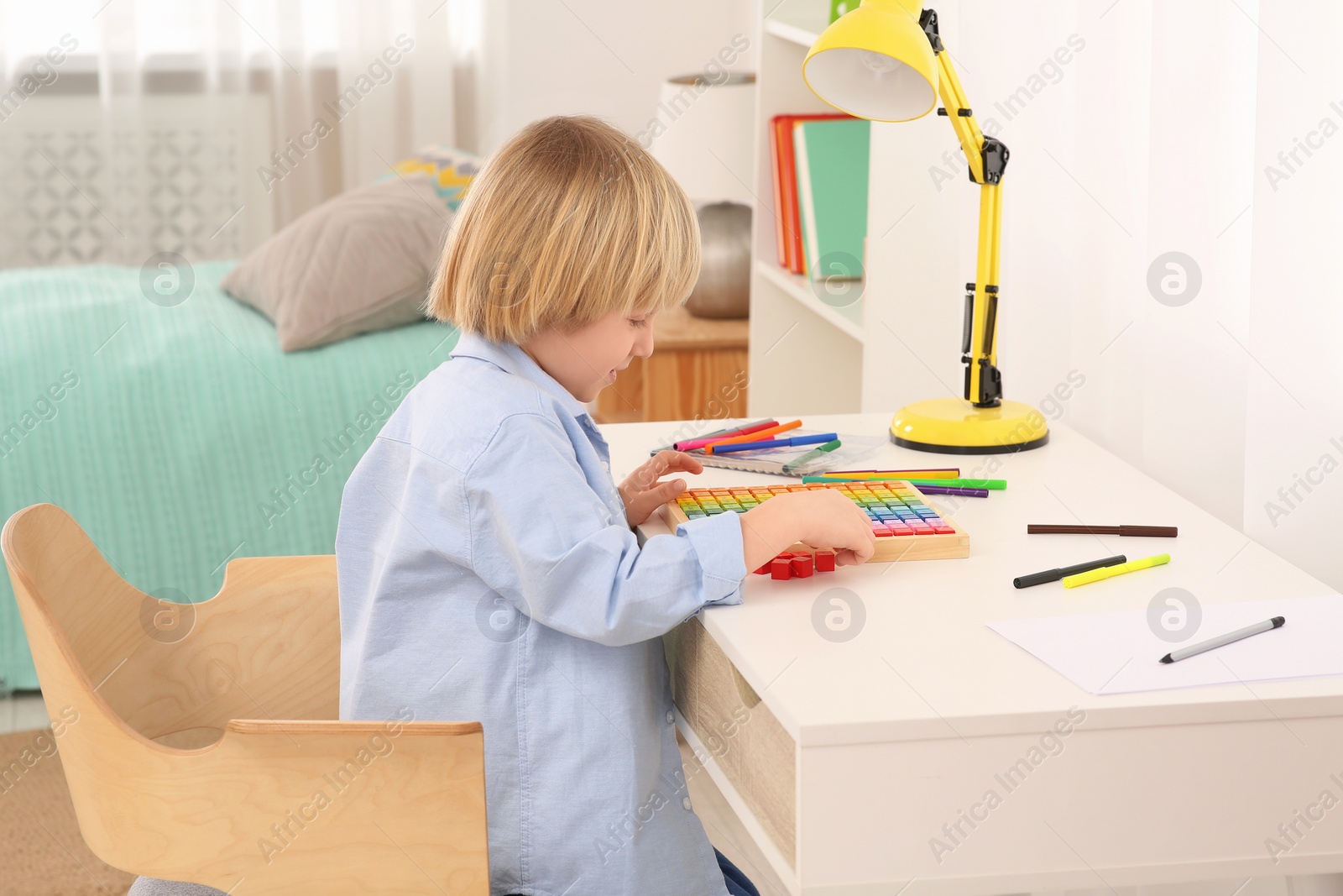 Photo of Cute little boy playing with colorful wooden cubes at desk in room. Home workplace