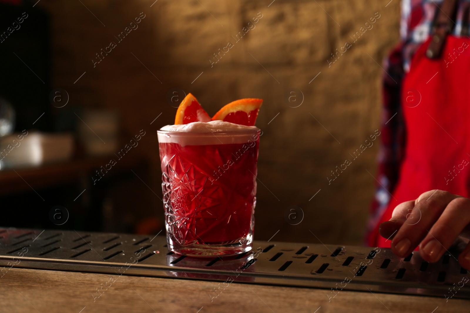 Photo of Glass of fresh alcoholic cocktail and bartender at bar counter, closeup