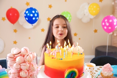 Photo of Cute little girl blowing out candles on her birthday cake indoors