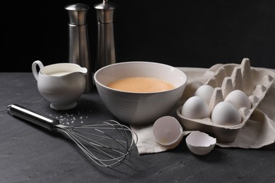 Photo of Metal whisk and dough ingredients on dark grey table