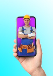 Woman with smartphone calling professional repairman on color background, closeup