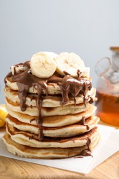 Photo of Tasty pancakes with sliced banana served on wooden board, closeup