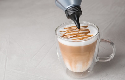 Photo of Adding caramel topping to latte macchiato on table, space for text