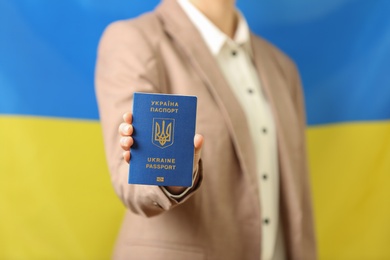 Woman holding Ukrainian travel passport against national flag, closeup. International relationships