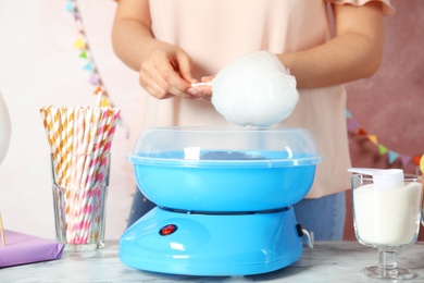 Woman making cotton candy using modern machine at table, closeup