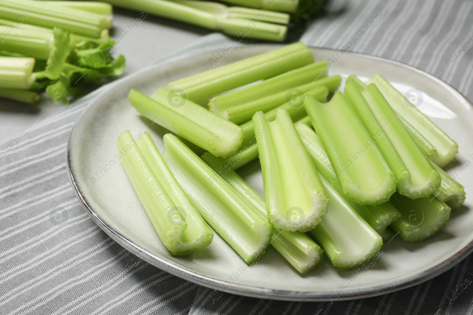 Photo of Fresh green cut celery on striped tablecloth, closeup