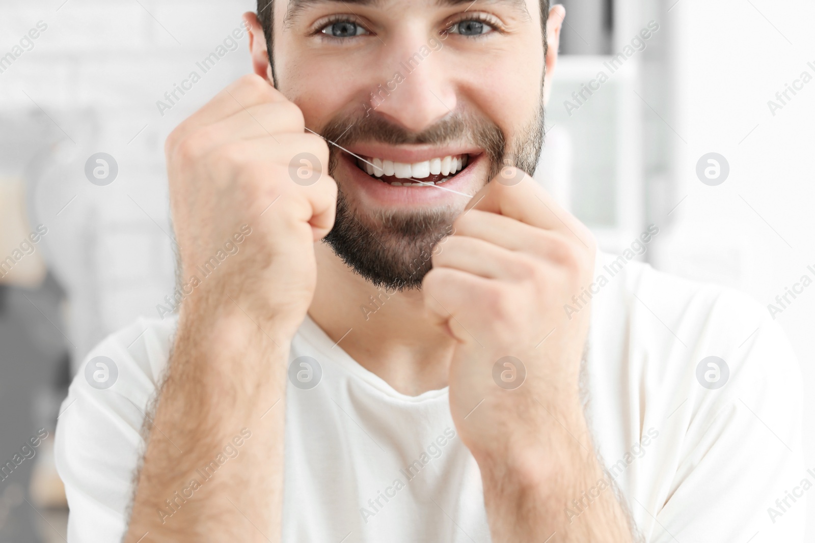 Photo of Young man flossing his teeth indoors