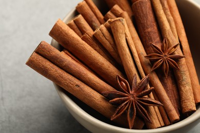 Photo of Bowl of cinnamon sticks and star anise on grey table, closeup