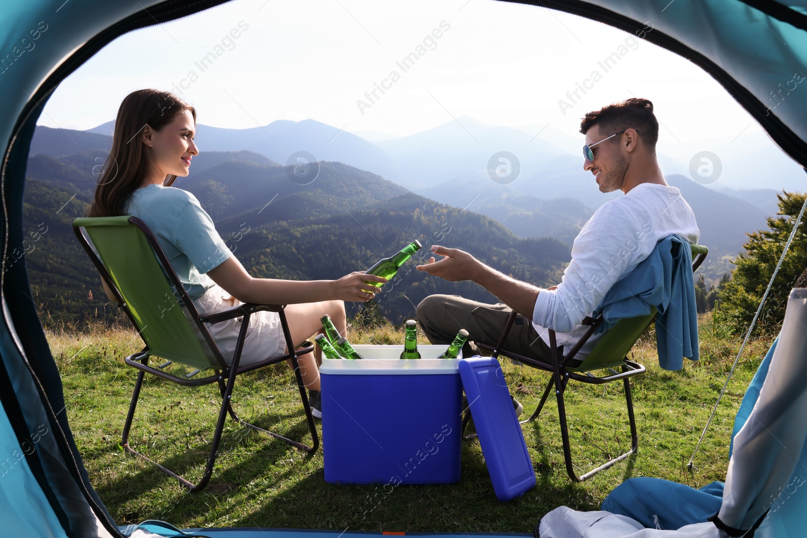 Photo of Couple and cool box with bottles of beer in mountains, view from tent