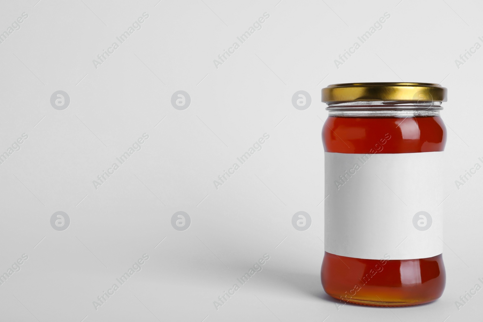 Photo of Glass jar of wildflower honey with blank label isolated on white