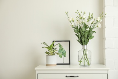 Photo of Decorative vase with flowers and houseplant on commode indoors