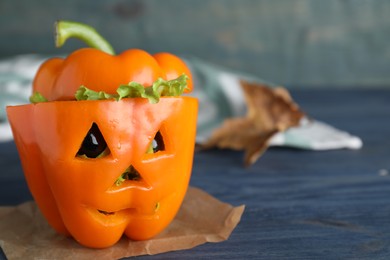 Photo of Bell pepper with black olives and lettuce as Halloween monster on blue wooden table. Space for text
