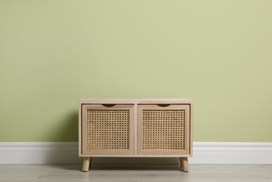 Photo of Modern wooden chest of drawers near light green wall indoors