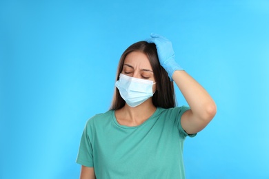 Stressed woman in protective mask on light blue background. Mental health problems during COVID-19 pandemic