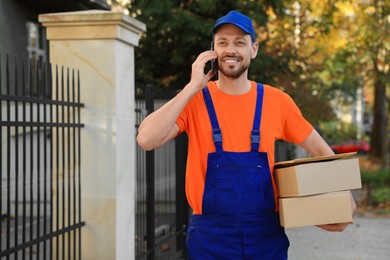 Photo of Courier with parcels talking on smartphone outdoors, space for text. Order delivery