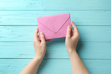 Photo of Woman with pink paper envelope at light blue wooden table, top view