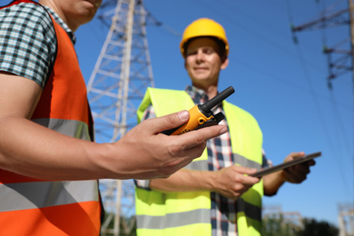Photo of Professional electricians near high voltage towers, focus on hand with portable radio station