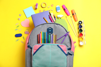 Photo of Stylish backpack with different school stationery on yellow background, flat lay