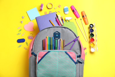 Stylish backpack with different school stationery on yellow background, flat lay