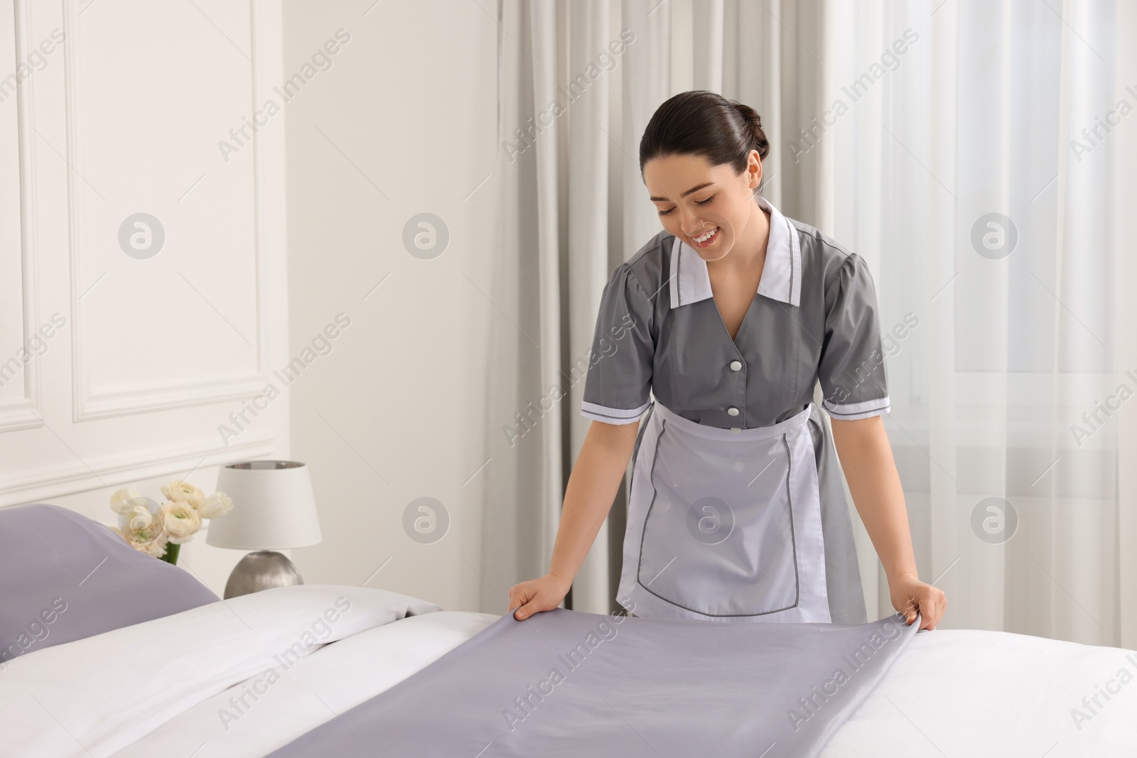 Photo of Young chambermaid making bed in hotel room