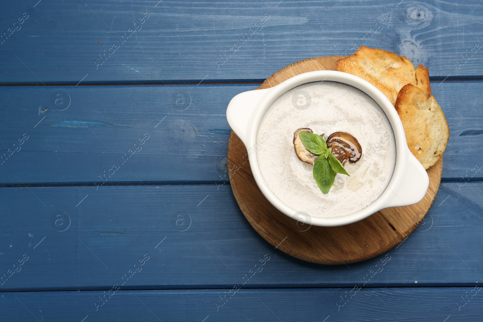Photo of Fresh homemade mushroom soup in ceramic pot on blue wooden table, top view. Space for text