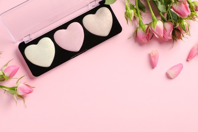 Photo of Palette of heart shaped eyeshadows and roses on light pink background, flat lay. Space for text