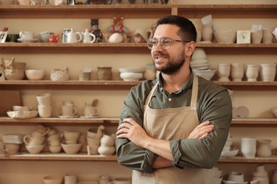 Photo of Portrait of smiling craftsman near shelf with different pottery in workshop. Space for text