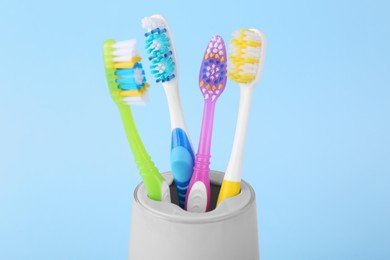 Photo of Different toothbrushes in holder on light blue background, closeup