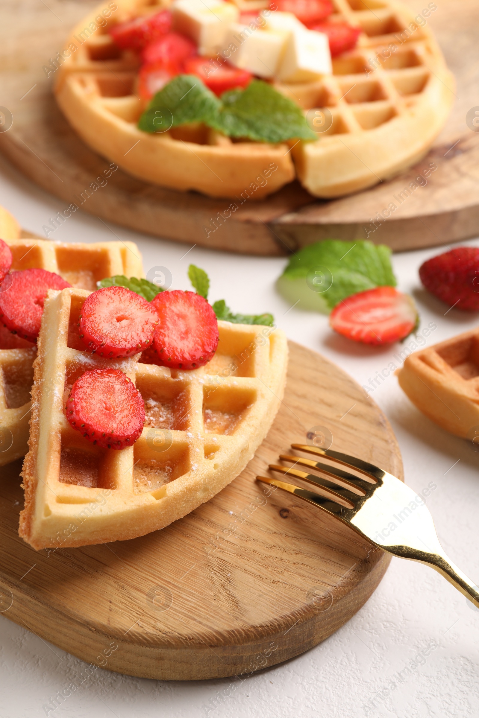Photo of Tasty Belgian waffles with strawberries, mint and fork on white table, closeup