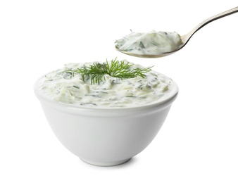 Photo of Spoon and bowl of cucumber sauce on white background. Traditional Tzatziki