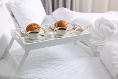 Photo of Tasty breakfast served in bed. Fresh croissants, coffee and honey on tray