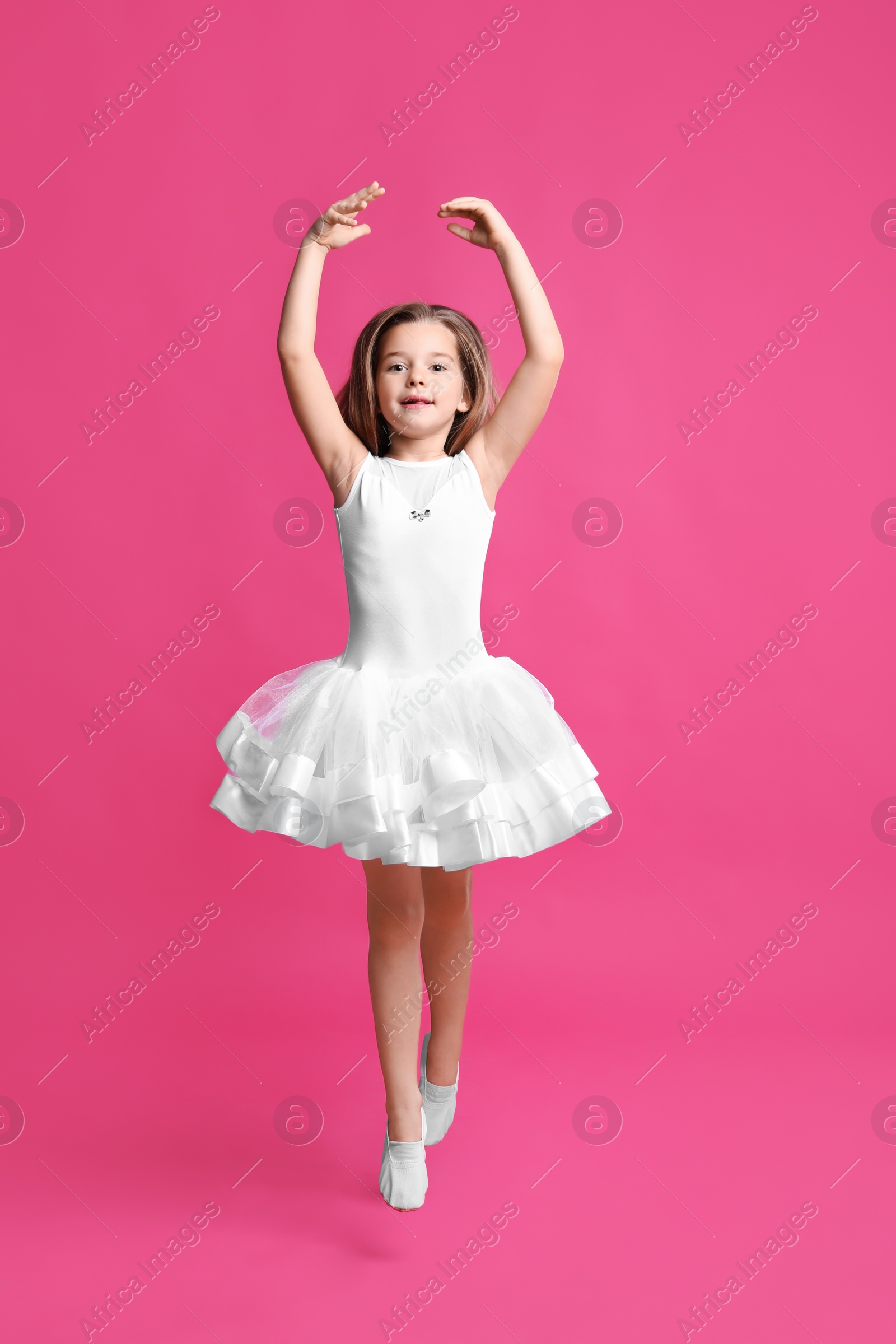 Photo of Cute little girl in white dress dancing on pink background