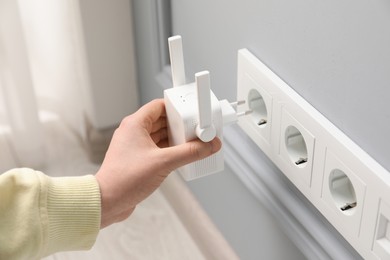 Photo of Woman inserting wireless Wi-Fi repeater into power socket indoors, closeup