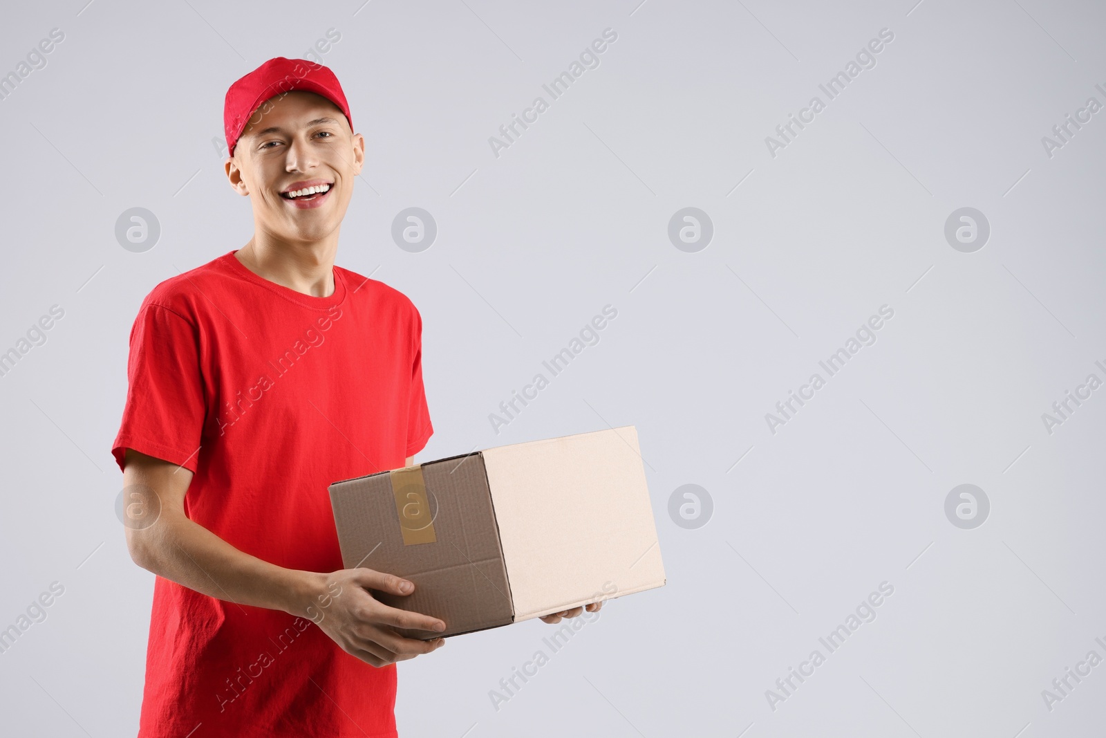 Photo of Happy courier with parcel on light grey background. Space for text