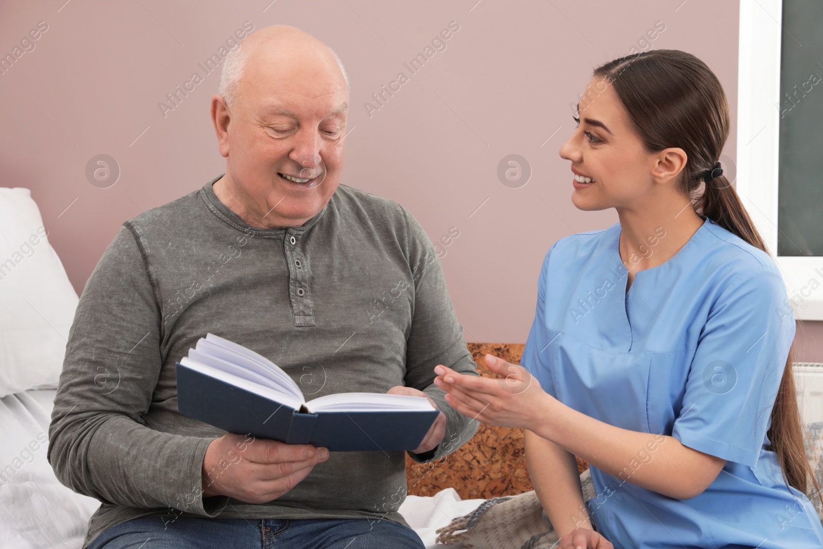 Photo of Nurse reading book with senior man in hospital ward. Medical assisting