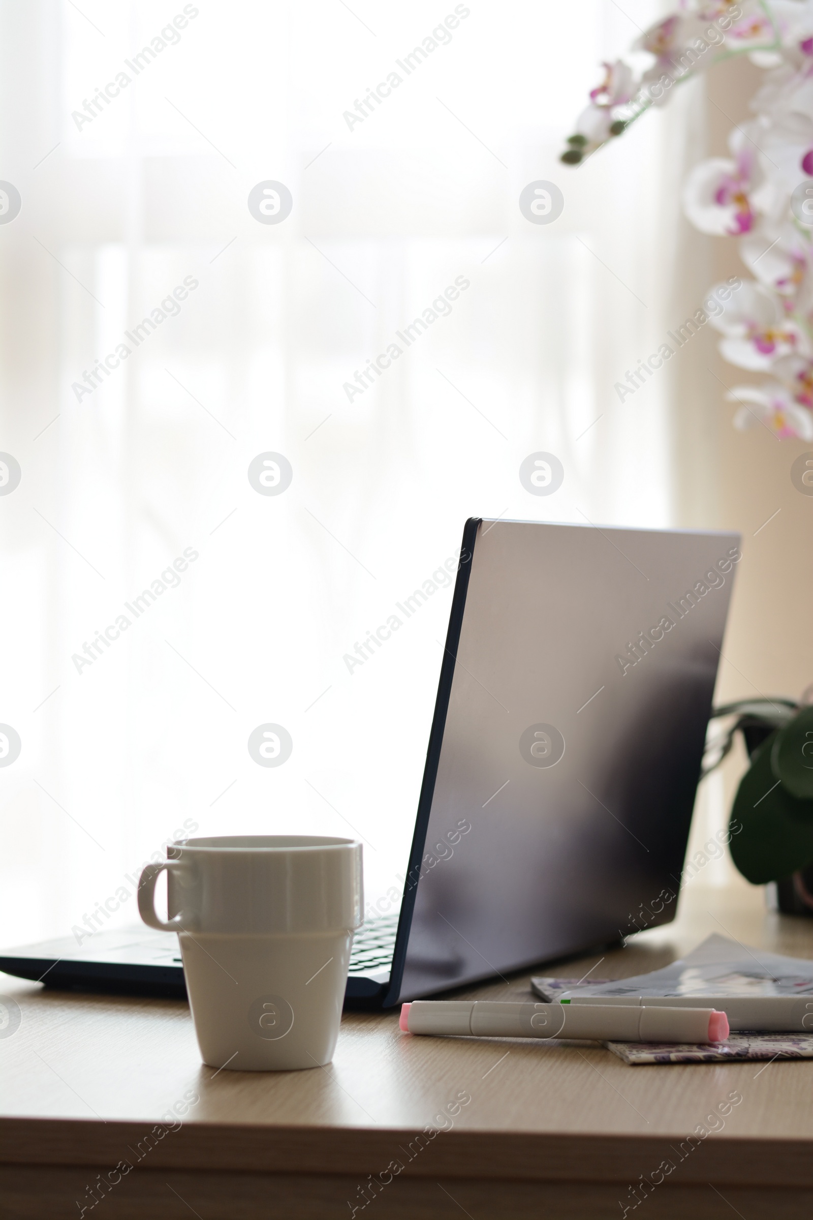 Photo of Ceramic cup, laptop and stationery on wooden table indoors. Good morning