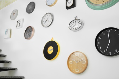 Many different clocks hanging on white wall. Time of day