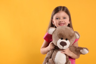 Cute little girl with teddy bear on yellow background. Space for text