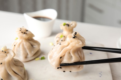 Chopsticks with tasty baozi dumpling over table, closeup