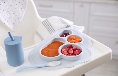 Photo of High chair with food in baby tableware on white tray indoors, closeup